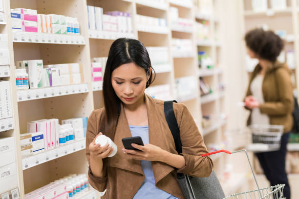 asiática mujer comprobación suplemento en smartphone en farmacia - pill bottle pharmacy medicine shelf fotografías e imágenes de stock