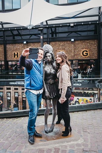 London, UK - March 23, 2019: Tourists taking photos with Amy Winehouse statue in Camden, London. Sculpted by Scott Eaton, it was unveiled in 2014, three years after the singer's death.
