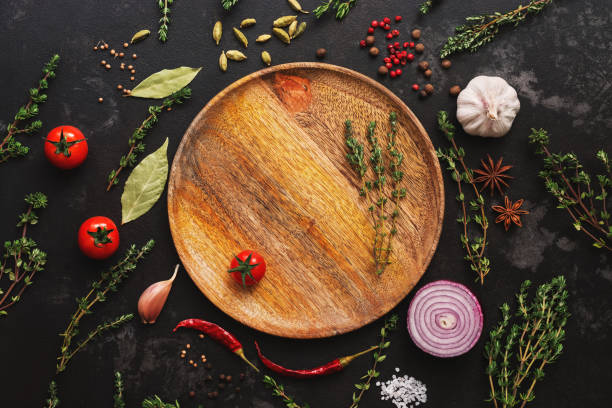 istock Different seasoning for cooking on a dark background. Empty wooden plate, spices, herbs, vegetables. Top view, flat lay. 1138458164