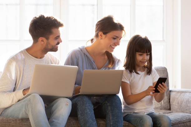 istock Smiling family sitting on couch absorbed in digital devices 1138470066