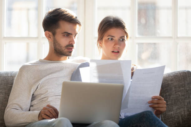 sorprendido por las malas noticias de la pareja sentada en el sofá leyendo carta - bank statement fotos fotografías e imágenes de stock