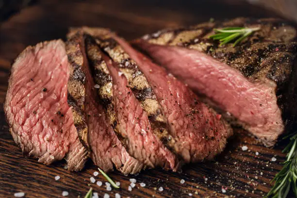 Juicy medium Beef Rib Eye steak slices on wooden board with herbs spices and salt. Ready to eat steak with ingredients on a cutting board.