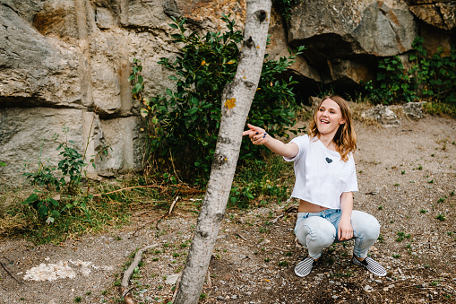 Girl sitting and poses with imaginary pistol. Portrait of a joke woman against background of the mountain on nature. Close up. grimace. makes a shot with his hand.