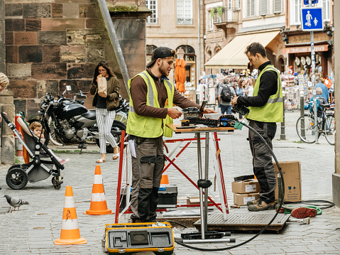 Paris, France - June 13, 2018: Team working near open sewage manhole hole - internet provider working on implementation of fiber optic cables in French city public network infrastructure