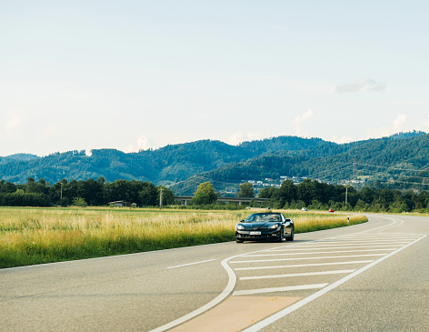 Schiltach, Germany - Jun 10, 2018: German highway with luxury Chevrolet Corvette convertible cabriolet car driving fast on the rural highway on a sunny day with Black Forest mountains in background