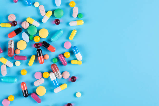 medicine green, yellow, red and pink pills or capsules on a blue background with copy space. - antibiotic red medicine healthcare and medicine imagens e fotografias de stock