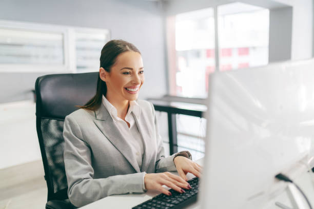 istock Smiling secretary dressed in formal wear typing on keyboard e-mail while sitting in office. It's not about being the best. It;s about being better than you were yesterday. 1138482989