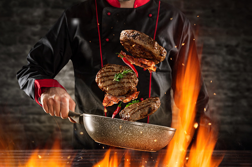 Closeup of chef throwing hamburger steaks into the air. Concept of food preparation, grill and barbecue
