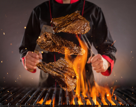 Flying beef steaks above the grill with chef on background. Concept of food preparation, grill and barbecue