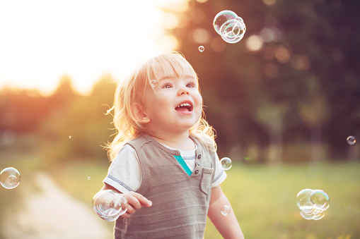 Cute little child playing with soap bubbles in a park.