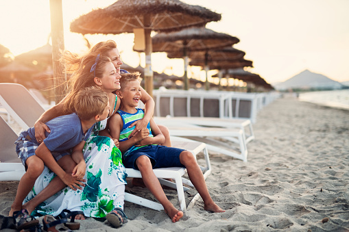 Happy family sitting on beach sunbeds, relaxing, laughing and looking at the sea.\nNikon D850