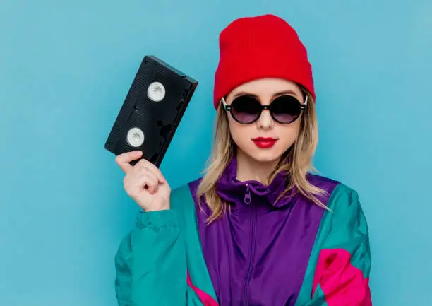 Photo of woman in red hat, sunglasses and suit of 90s with VHS cassette