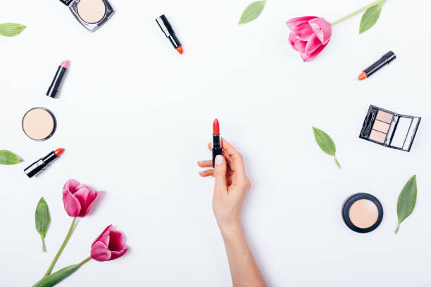 Woman's hand holding open classic red lipstick Woman's hand holding open classic red lipstick among decorative cosmetics and fresh flowers on white table, top view. Flat lay composition of pink tulips and feminine makeup beauty products. person holding frame over face stock pictures, royalty-free photos & images