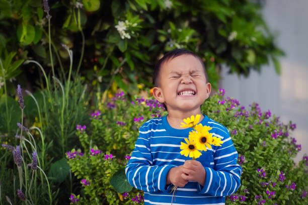 A cheerful young boy holding a few hand picked yellow flowers during spring time, standing in front of a lush garden. stock photo