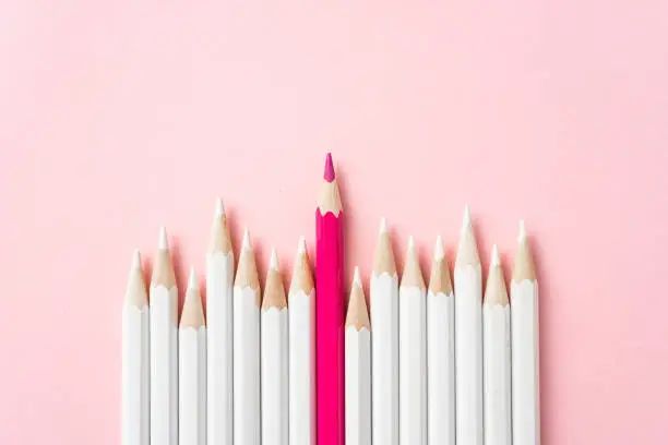 Business and design concept - lot of white pencils and one color pencil on pink paper background. It's symbol of leadership, teamwork, success and unique.