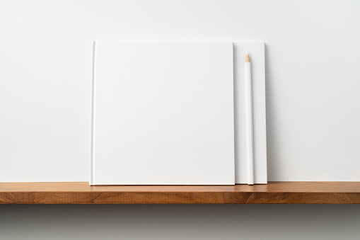 Design concept - front view of two square white notebook on bookshelf and white wall for mockup