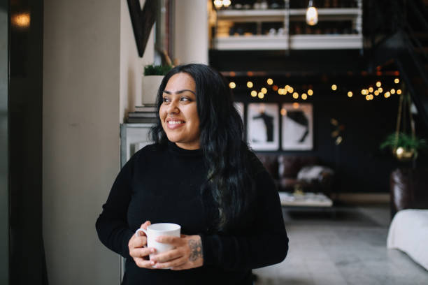 Portrait of a young woman having coffee in her Downtown Los Angeles apartment Young woman relaxing on the bed in her Downtown Los Angeles apartment, having an easy afternoon, drinking coffee. aborigine woman stock pictures, royalty-free photos & images