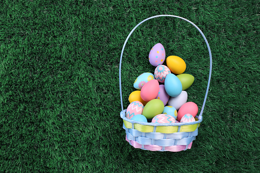 Easter eggs basket filled with colorful Easter eggs on green grass