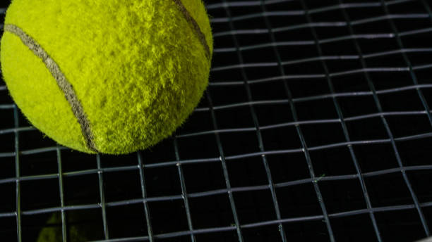feche acima da esfera de tênis verde acima da corda preta da raquete isolada no preto - racket string - fotografias e filmes do acervo