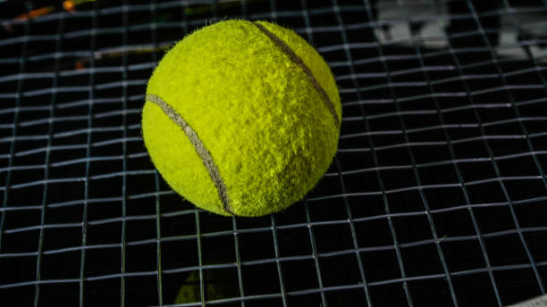 gros plan de balle de tennis vert au-dessus de la chaîne de raquette noire isolé en noir - racket string photos et images de collection