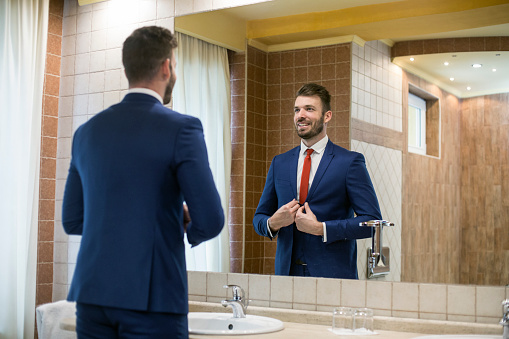Adult businessman in a luxury hotel bathroom, fixing his suit. About 25 years old, Caucasian male.