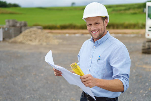 Handsome architect or site supervisor Handsome architect or supervisor standing outdoors on a building site holding a blueprint in his hands looking at the camera with a friendly smile foreperson stock pictures, royalty-free photos & images
