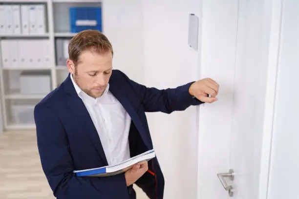 Young businessman knocking on the door of the boss as he stands outside looking down at a folder in his hand