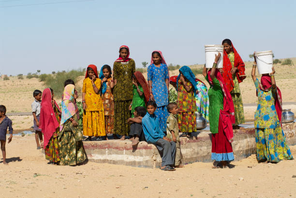 groupe de jeunes femmes et les enfants portant des robes traditionnelles recueillir l'eau d'un côté de la route publique bien dans le désert du grand thar à jamba, en inde. - india rajasthan thar desert travel photos et images de collection
