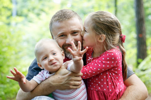 Devoted father hugging his son and daughter, enjoying the outdoor. Devoted father hugging his son and daughter, enjoying the outdoor. Family love and bonding, active lifestyle, fathers day concept. real life photos stock pictures, royalty-free photos & images