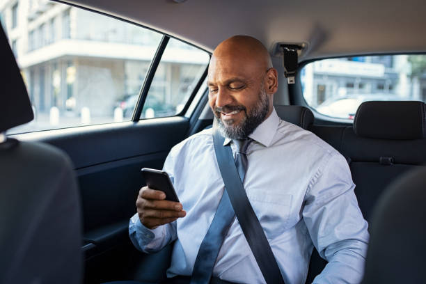 Mature business man using phone in car Successful african businessman working on phone smiling witting in car. Portrait of mature smiling business man in formal clothes using smartphone while sitting on back seat of luxury business car. Senior formal man reading confirmation mail on smartphone and smiling in a taxi. back seat photos stock pictures, royalty-free photos & images