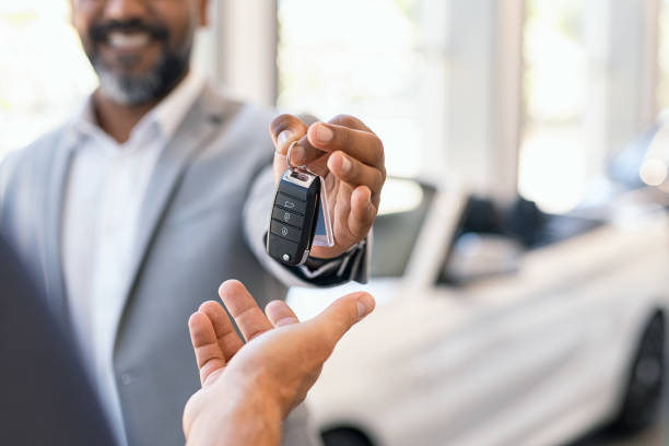 Salesman giving new car keys to customer Closeup hand of cardealer giving new car key to customer. Detail of salesman hand giving keys to a client at showroom. Man's hand receiving car keys from african agent in a auto dealership with copy space. car dealership stock pictures, royalty-free photos & images