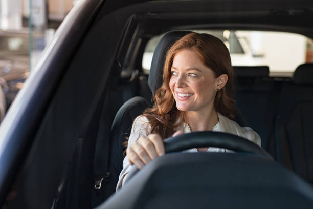 Young woman driving car Mature beautiful woman sitting in car looking away while trying new automobile. Portrait of daydreaming mature woman doing drive test of new car. Cheerful smiling lady enjoying driving while looking away. driver occupation stock pictures, royalty-free photos & images