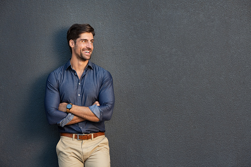 Happy successful businessman in smart casual clothing looking away. Portrait of satisfied business man with crossed arms isolated over grey background with copy space. Handsome young man smiling against grey wall.
