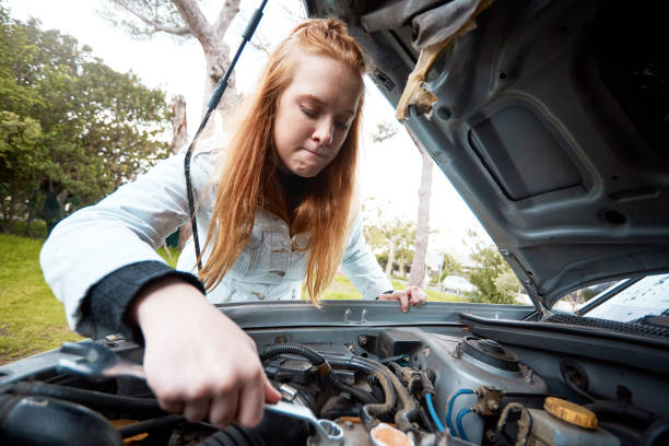 istock Confused and irritated young redhead attempts to fix her car 1138562735