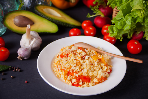 Homemade vegetarian couscous with tomatoes, carrots, pepper on a dark kitchen table with vegetables on the background
