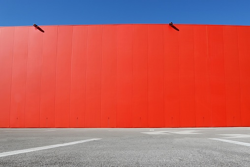 Bright red aluminium cladding wall with an asphalt road in front. Background for copy space.