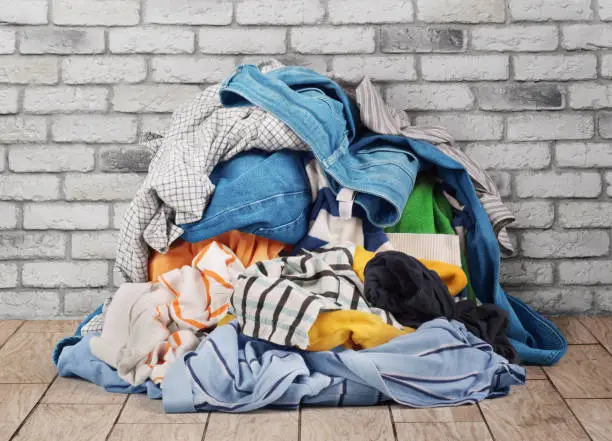 Photo of Pile of clothes on floor near brick wall