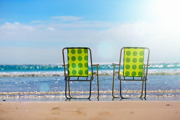 Two empty beach chairs sit next to a calm, sunlit sea enjoying an idyllic holiday.