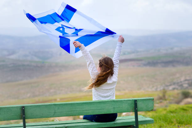 Israeli jewish little girl with Israel flag back view. Beautiful young jewish girl sitting holding Israel flag in the wind and enjoying great view landscape on the sky, field and mountains.Patriotic holiday. Independence day Israel - Yom Ha'atzmaut . gaza strip photos stock pictures, royalty-free photos & images