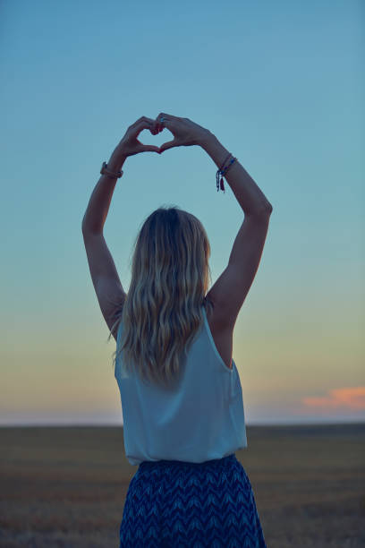 menina que prende o símbolo da coração-forma para o amor no por do sol/nascer do sol tempo. - heart shape loneliness women praying - fotografias e filmes do acervo