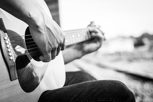Playing on acoustic guitar outdoor. Black and white photo