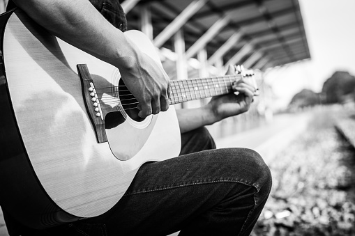 Playing on acoustic guitar outdoor. Black and white photo