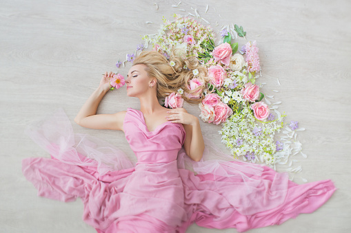 TOP VIEW: Portrait of a young girl with a closed eyes in a pink dress on a floor with a flowers