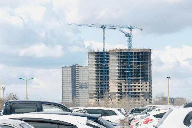 Modern building under construction parking in the foreground and the construction of high-rise buildings in the background using a high-rise crane clouds sky