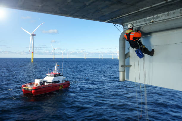 Rope access technician making inspection, repairing on offshore platform with transfer vessel guarding stock photo