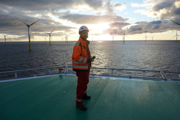 Offshore manual worker standing on helipad with wind-turbines behind him in sunset stock photo