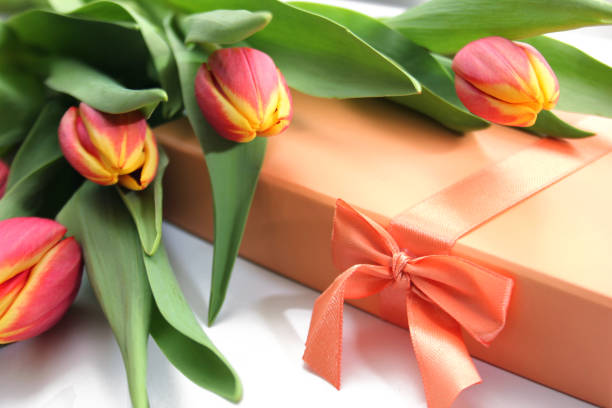 A composition of orange yellow tulips and a gift box with a orange ribbonloop.