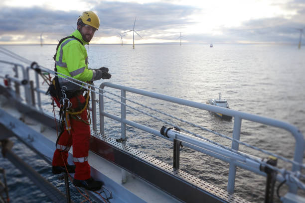 Rope access technician making inspection and repairs of railing with transfer vessel guarding stock photo