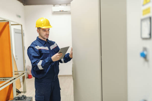 istock Caucasian dedicated electrician in in uniform and helmet on head using tablet and opening door with dashboard while standing in control room in heavy industry plant. 1138604000