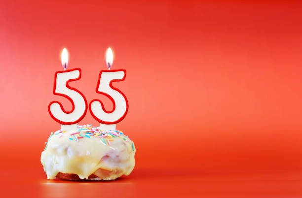 fünfundfünfzig jahre geburtstag. cupcake mit weißer brennender kerze in form der nummer 55. lebhafter roter hintergrund mit kopierraum - zahl 55 stock-fotos und bilder